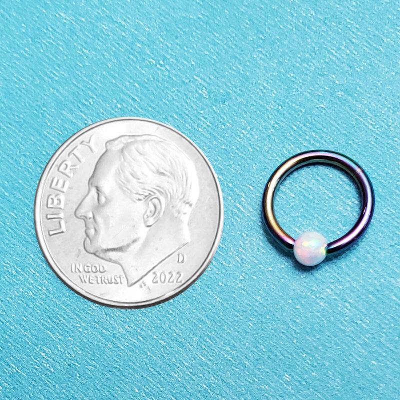 A rainbow opal captive septum ring pictured on an aqua background next to a dime for a size comparison.