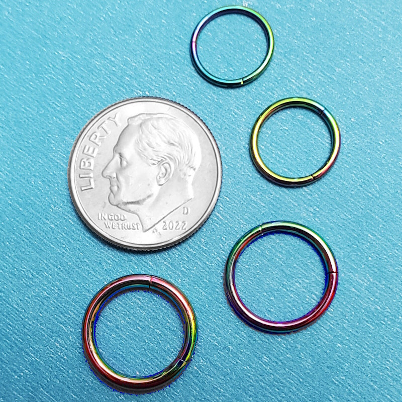 Four sizes of rainbow titanium septum rings pictured on an aqua background next to a dime for a size comparison.