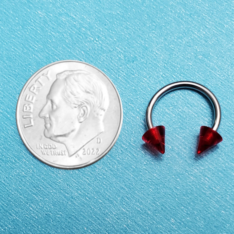 A red spike septum ring pictured on an aqua background next to a dime for a size comparison.