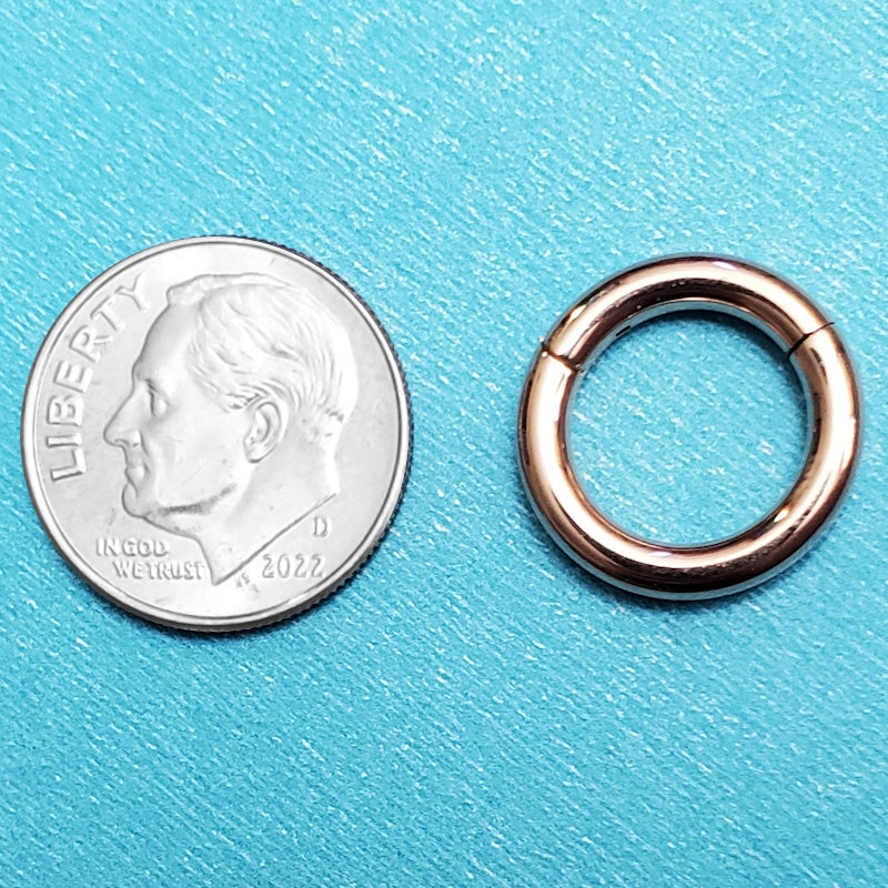 A rose gold 10g segment ring pictured on an aqua background next to a dime for a size comparison.