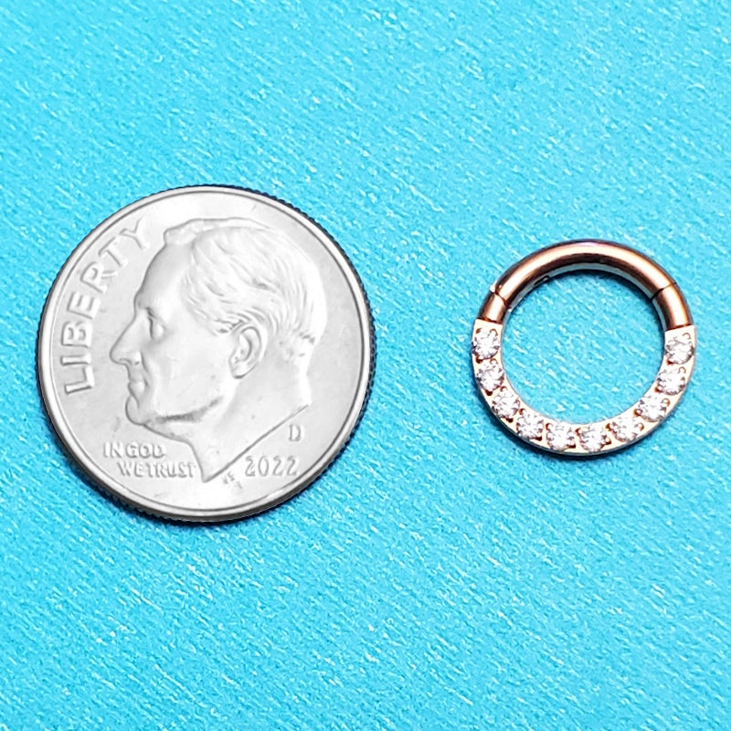 A rose gold 14g segment ring pictured on an aqua background next to a dime for a size comparison.