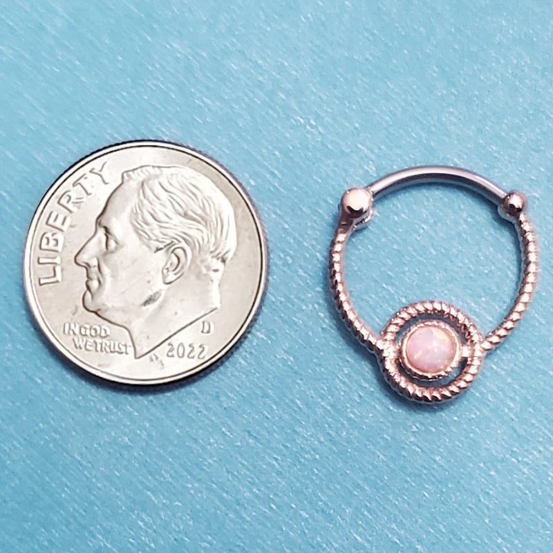 A rose gold clicker septum ring pictured on an aqua background next to a dime for a size comparison.