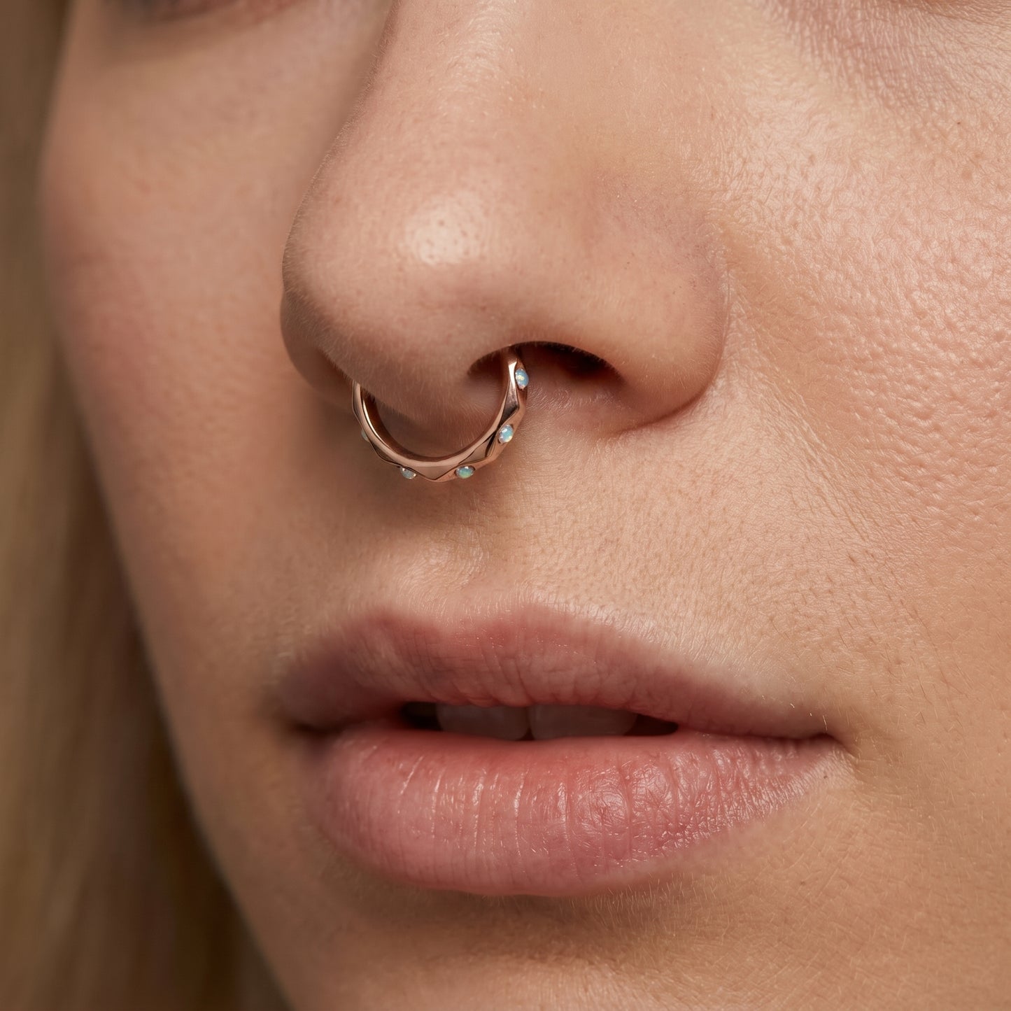 A Rose Gold Cubic Zirconia Segment Ring accented with diamond faceted cuts pictured in the septum piercing of a female model.