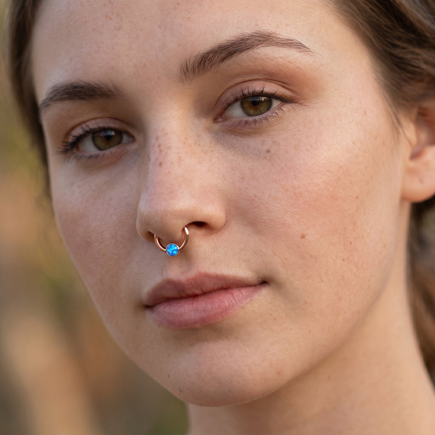A rose gold opal captive bead septum ring pictured in the septum piercing of a female model.