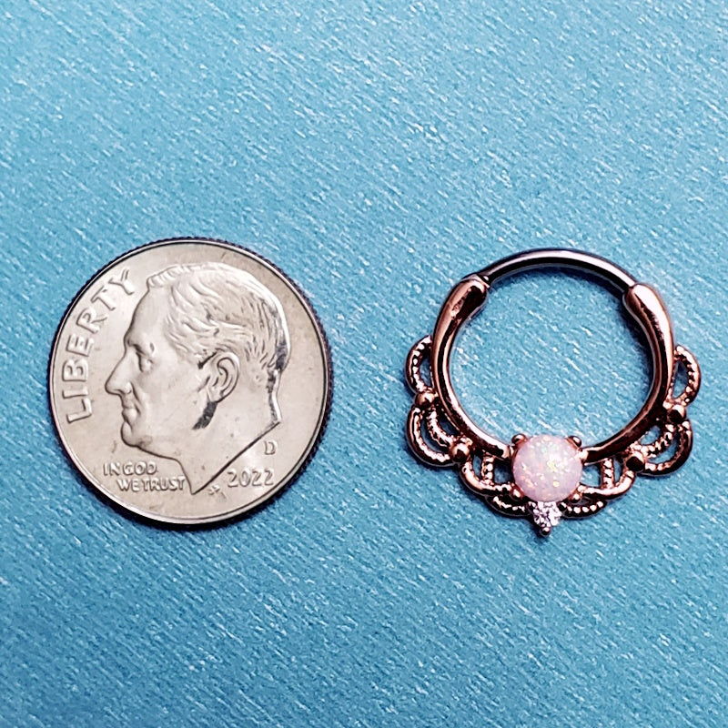 A rose gold septum clicker pictured on an aqua background next to a dime for a size comparison.