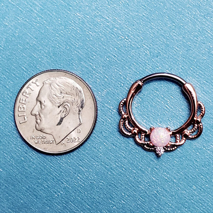 A rose gold septum clicker pictured on an aqua background next to a dime for a size comparison.