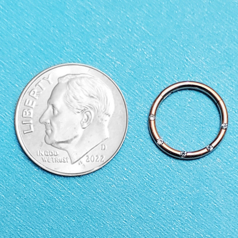 A rose gold septum piercing ring pictured on an aqua background next to a dime for a size comparison.