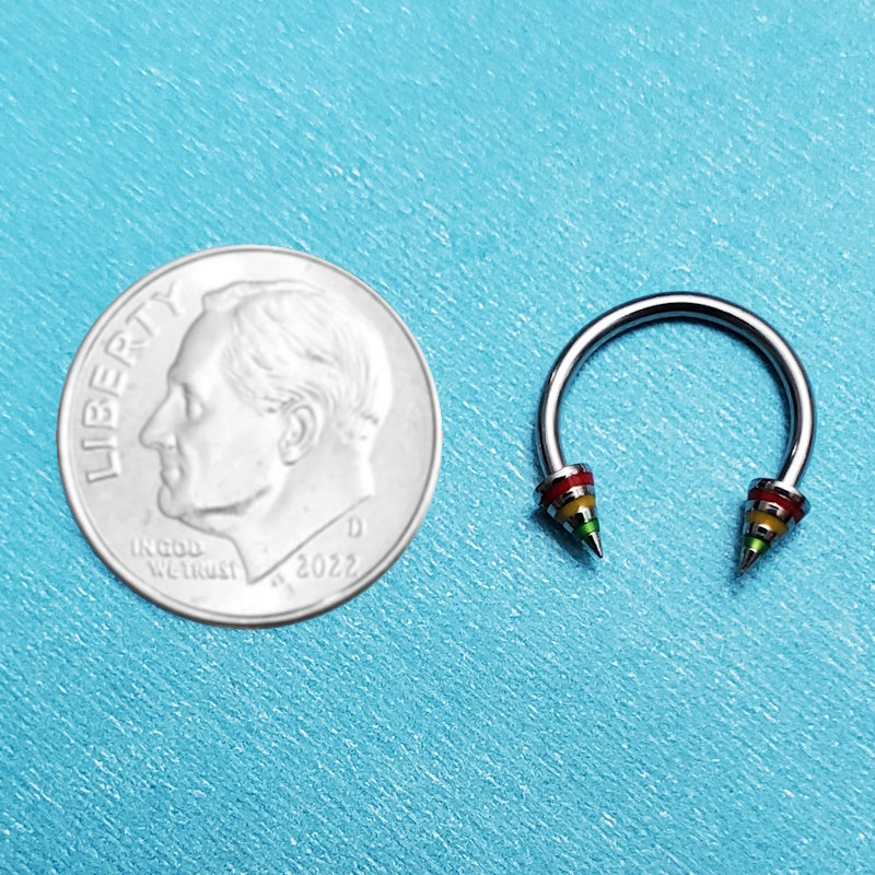 A spike rasta septum ring pictured on an aqua background next to a dime for a size comparison.