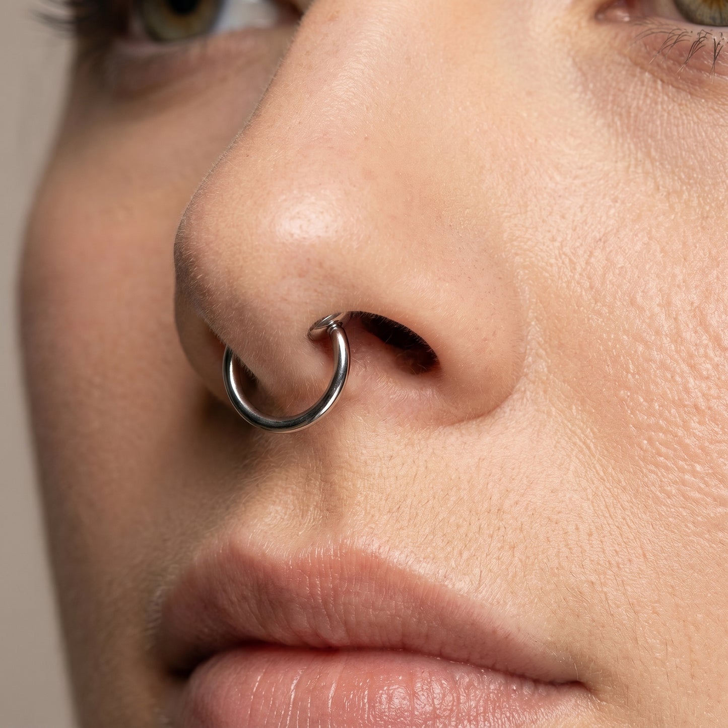 Spring Action Fake Septum Ring Titanium Plated 316L Surgical Steel pictured attached to the septum of a female model.