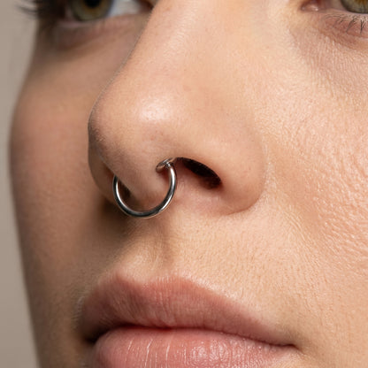 Spring Action Fake Septum Ring Titanium Plated 316L Surgical Steel pictured attached to the septum of a female model.