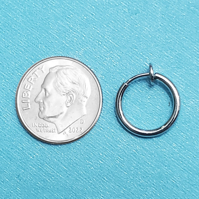 A spring action fake septum ring pictured on an aqua background next to a dime for a size comparison.