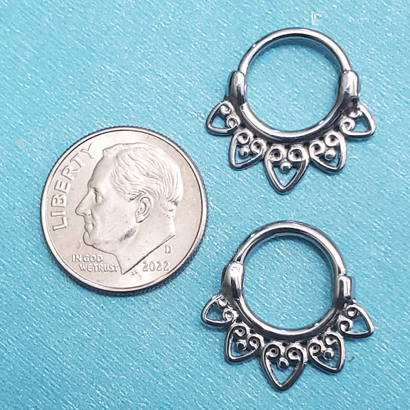 Two sizes of stainless steel septum clickers pictured on an aqua background next to a dime for a size comparison.