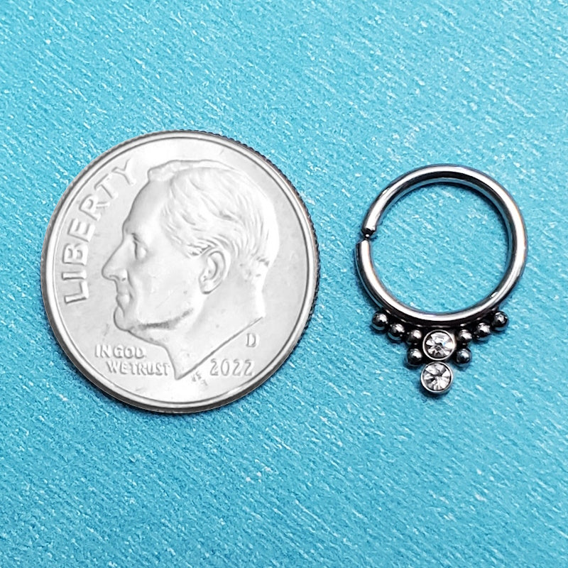 A surgical steel 16g septum ring pictured on an aqua background next to a dime for a size comparison.