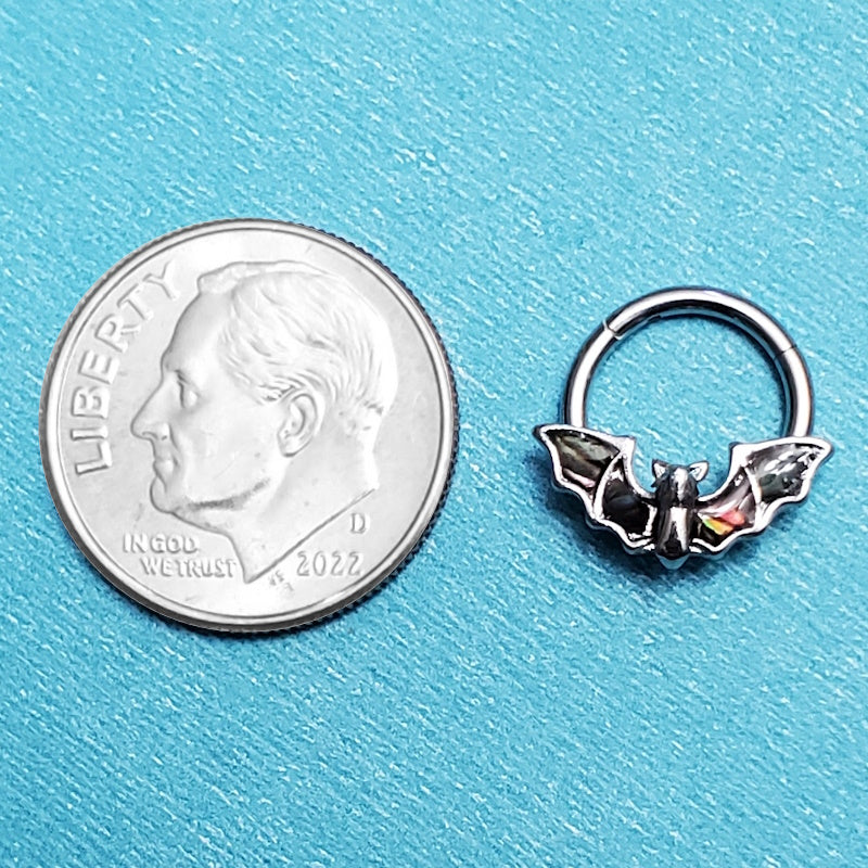 A surgical steel bat septum ring pictured on an aqua background next to a dime for a size comparison.