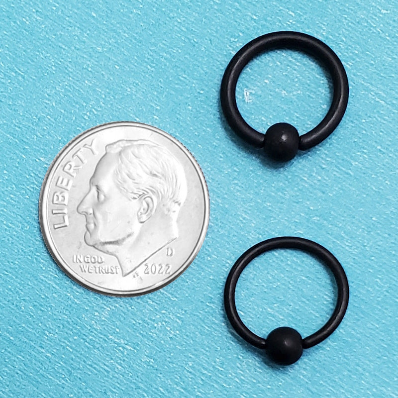 Two sizes of surgical steel black septum rings pictured on an aqua background next to a dime for a size comparison.