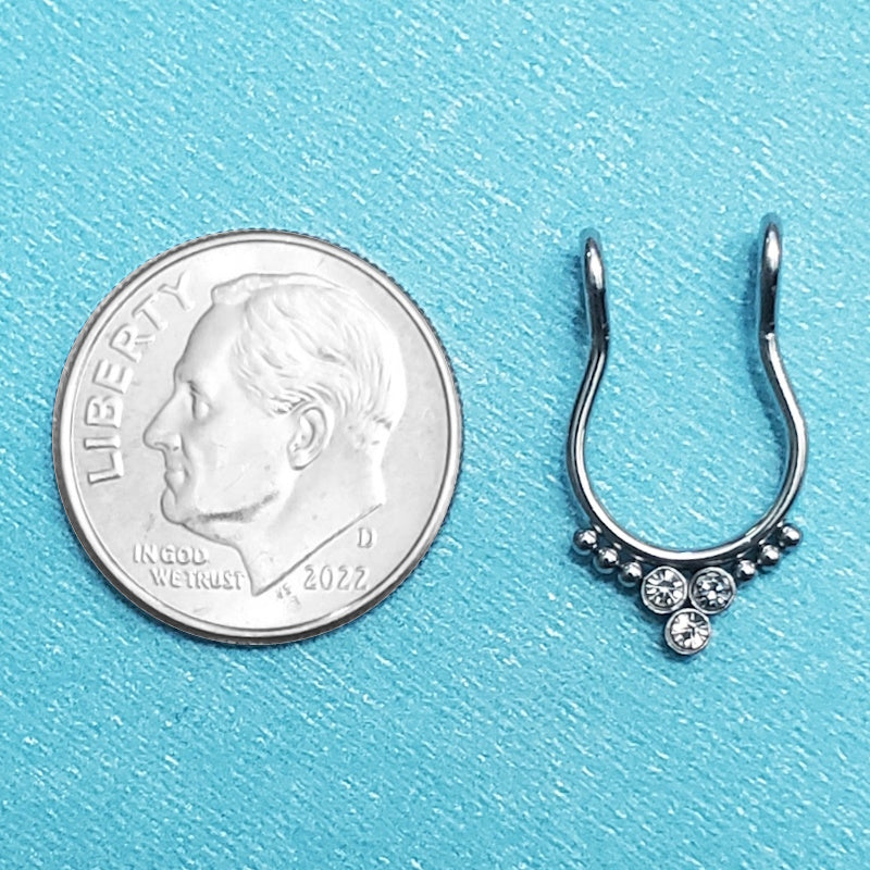 A surgical steel faux septum ring pictured on an aqua background next to a dime for a size comparison.