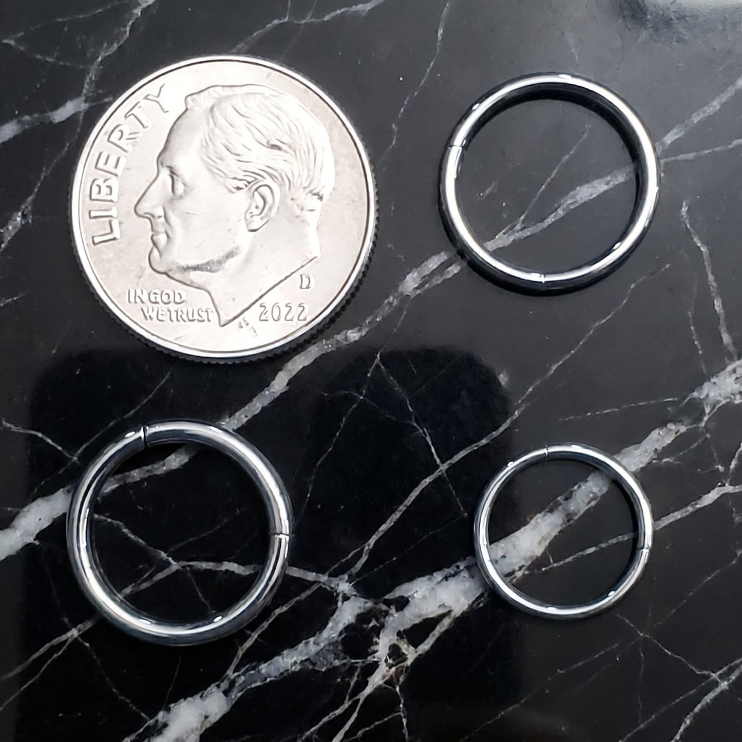 Hinged Segment Septum Ring 316L Surgical Steel 18G 16G 14G pictured on a black marble countertop next to a dime showing the size comparison.