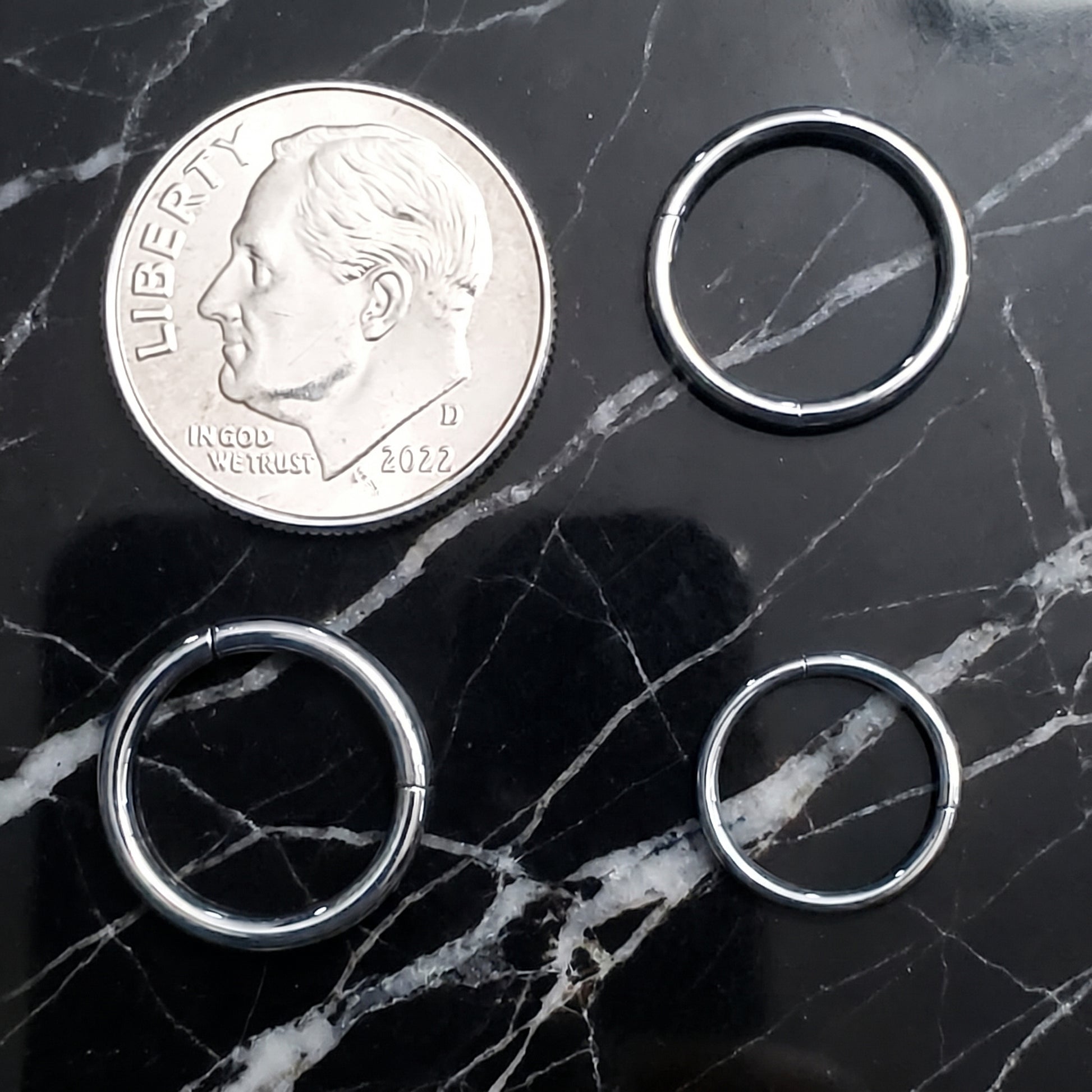 Hinged Segment Septum Ring 316L Surgical Steel 18G 16G 14G pictured on a black marble countertop next to a dime showing the size comparison.