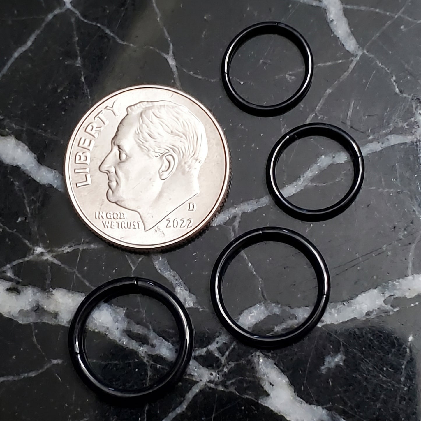 Black Hinged Segment Septum Ring 316L Surgical Steel 20G 18G 16G 14G pictured next to a US dime on a black marble countertop for a size comparison.