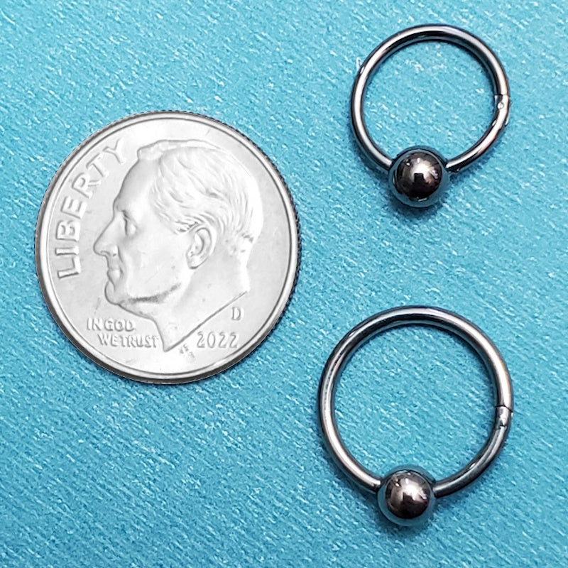 Two sizes of surgical steel hinged septum rings pictured on an aqua background next to a dime for a size comparison.