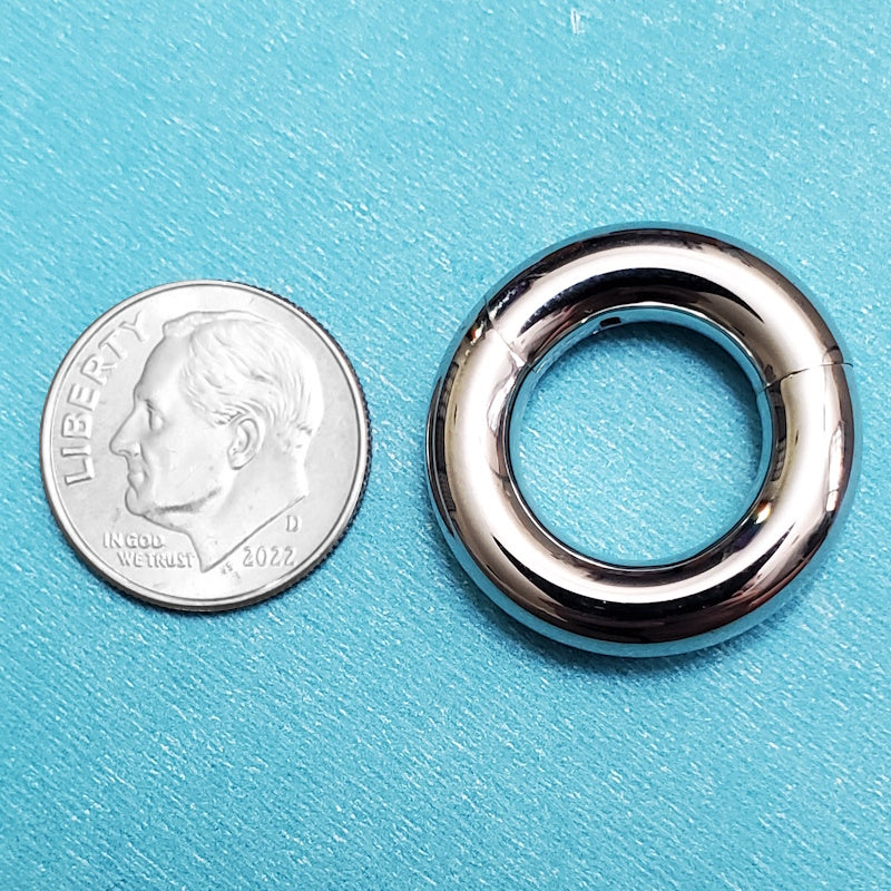 A surgical steel large septum ring pictured on an aqua background next to a dime for a size comparison.