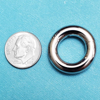 A surgical steel large septum ring pictured on an aqua background next to a dime for a size comparison.
