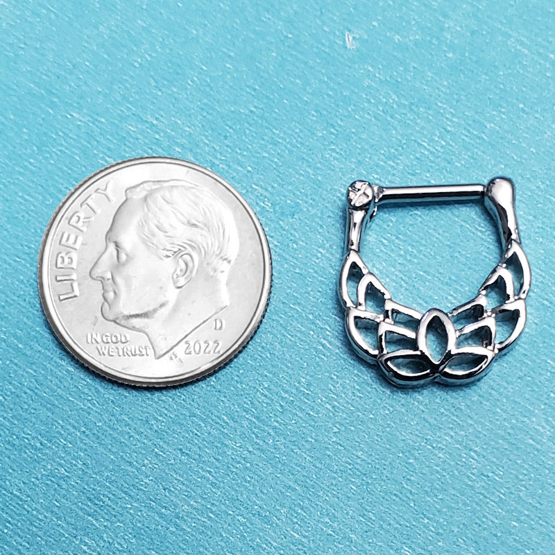 A 16 gauge surgical steel lotus septum clicker pictured on an aqua background next to a dime for a size comparison.