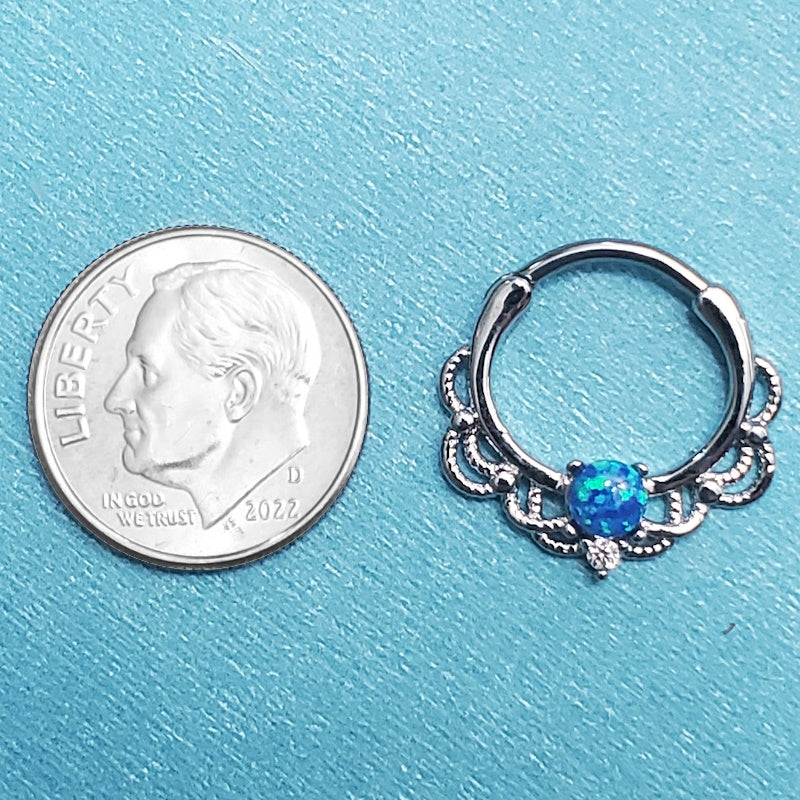 A surgical steel opal septum clicker pictured on an aqua background next to a dime for a size comparison.