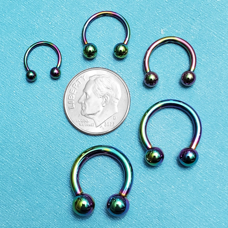 Five sizes of surgical steel rainbow septum rings pictured on an aqua background next to a dime for a size comparison.