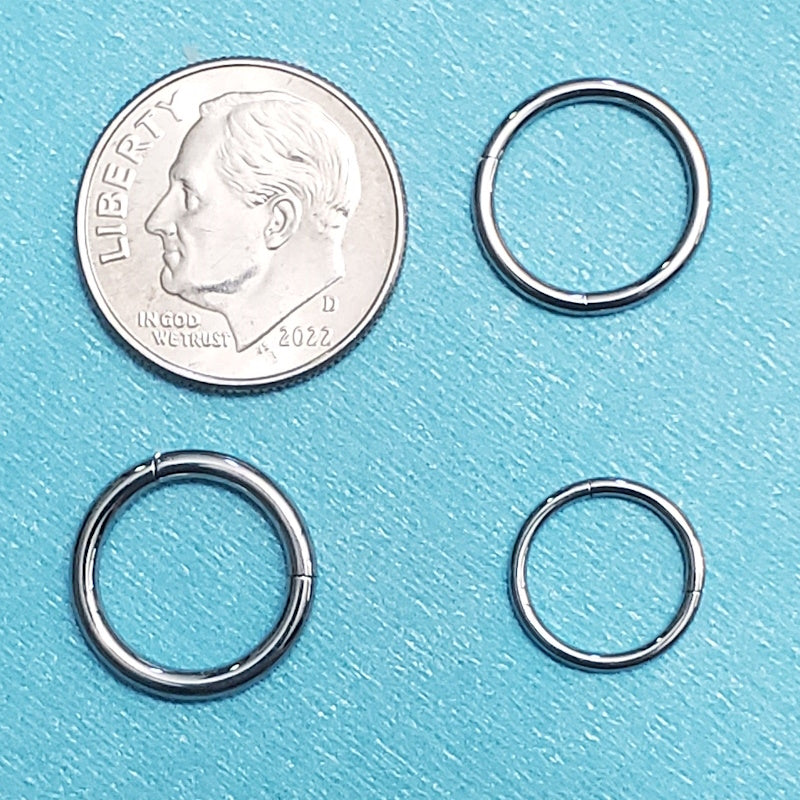 Three sizes of surgical steel segment rings pictured on an aqua background next to a dime for a size comparison.