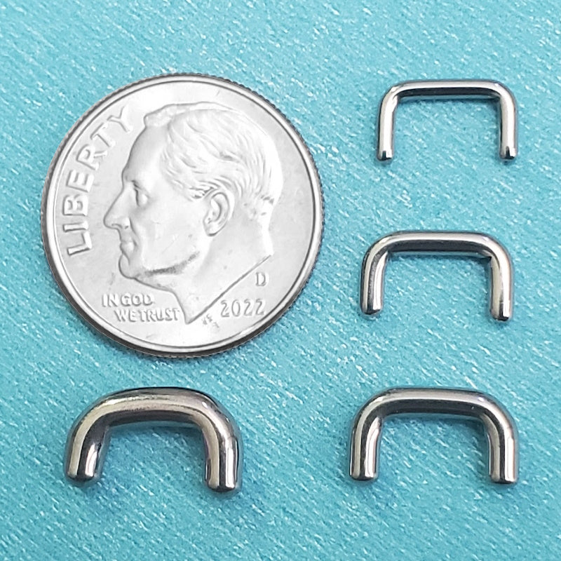 Four sizes of a surgical steel septum retainers pictured on an aqua background next to a dime for a size comparison.