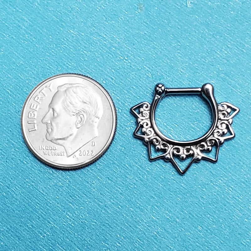 A surgical steel tribal septum ring pictured on an aqua background next to a dime for a size comparison.