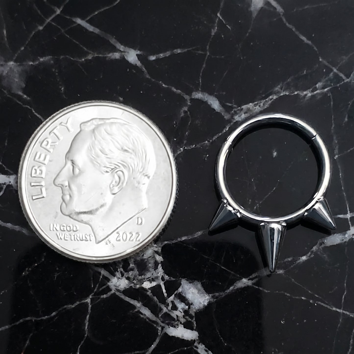 Three Spike Segment Septum Ring 16 Gauge ASTM F136 Titanium pictured on a black marble countertop next to a dime for size comparison.