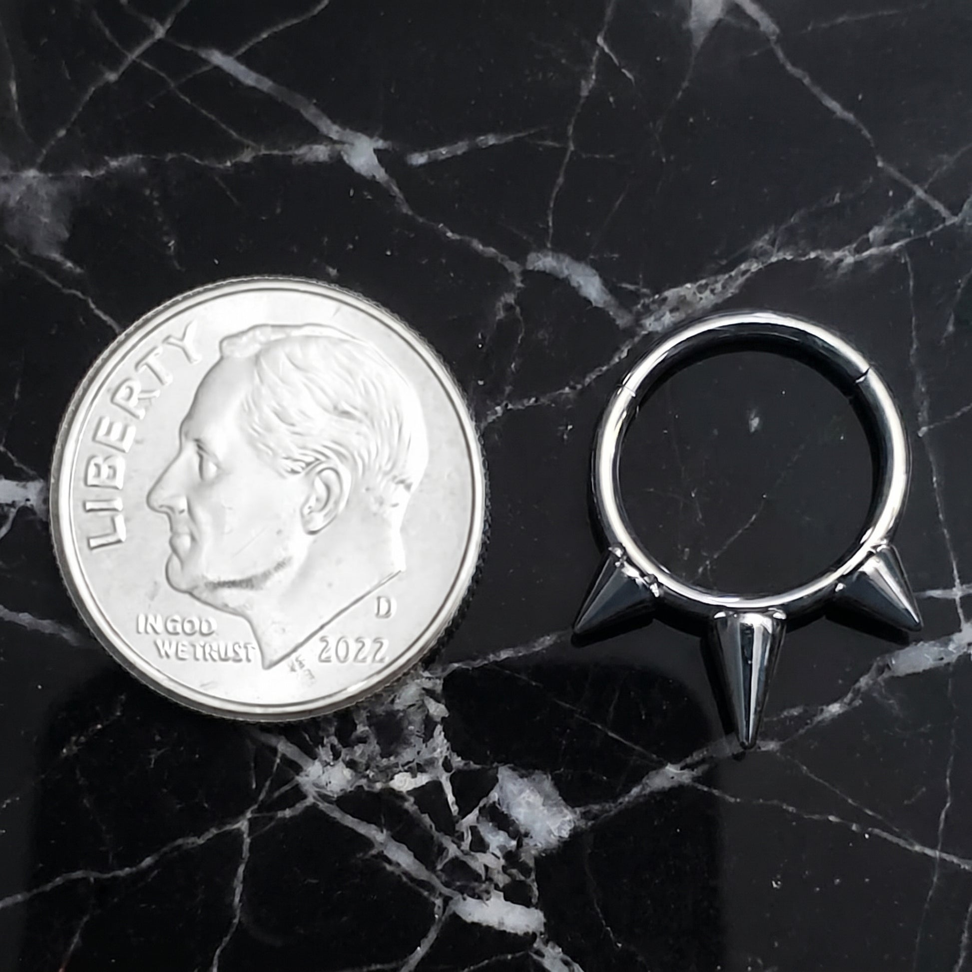Three Spike Segment Septum Ring 16 Gauge ASTM F136 Titanium pictured on a black marble countertop next to a dime for size comparison.