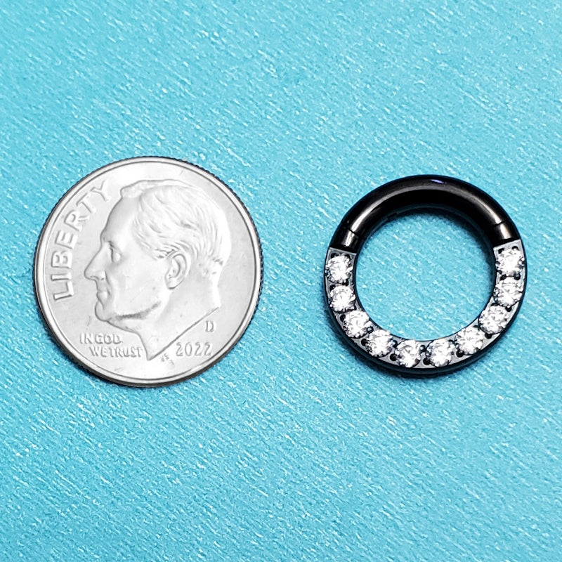 A titanium 10g septum ring pictured on an aqua background next to a dime for a size comparison.