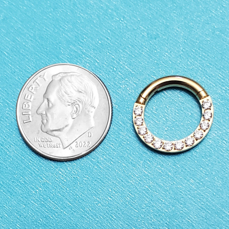 A titanium 12 gauge septum ring pictured on an aqua background next to a dime for a size comparison.