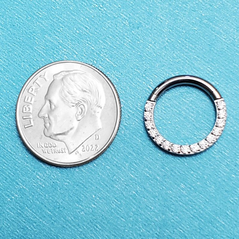 A titanium 14g septum ring pictured on an aqua background next to a dime for a size comparison.