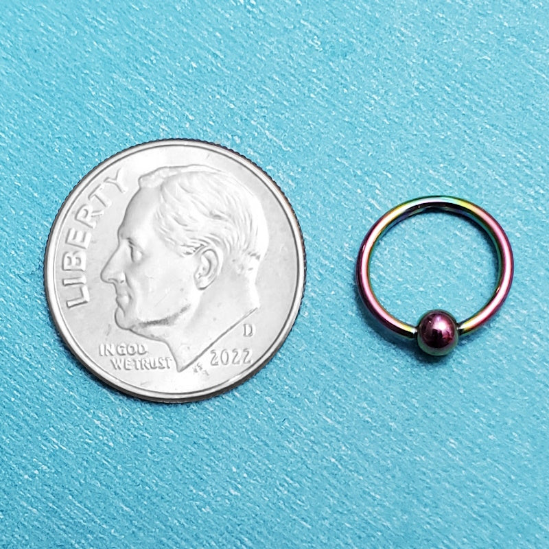 A titanium 18g septum ring pictured on an aqua background next to a dime for a size comparison.