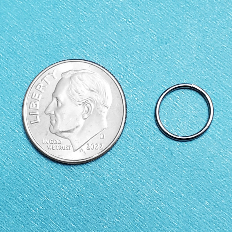 A titanium 20 gauge septum ring pictured on an aqua background next to a dime for a size comparison.