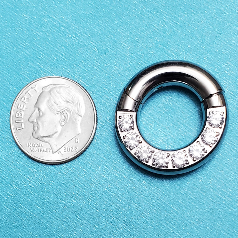 A titanium 4 gauge septum ring pictured on an aqua background next to a dime for a size comparison.