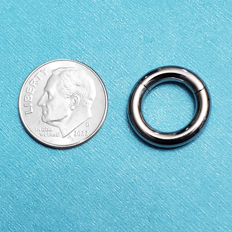 A titanium 8g segment ring pictured on an aqua background next to a dime for a size comparison.