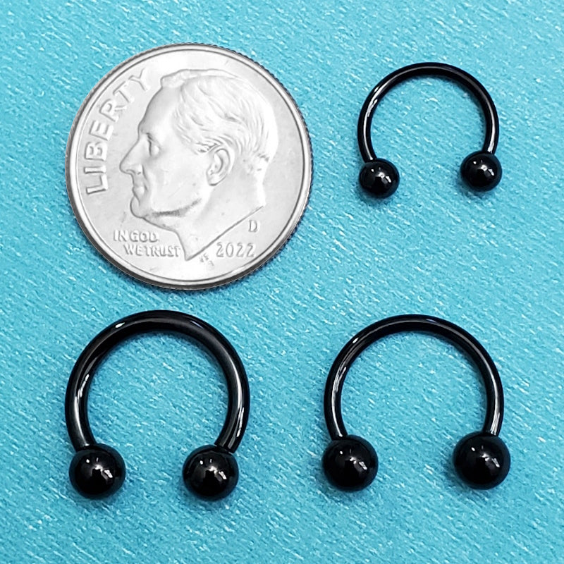 Three sizes of titanium black septum horseshoes pictured on an aqua background next to a dime for a size comparison.