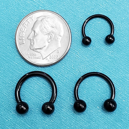 Three sizes of titanium black septum horseshoes pictured on an aqua background next to a dime for a size comparison.