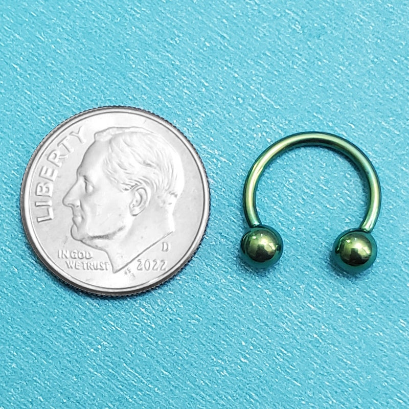 A titanium green septum ring pictured on an aqua background next to a dime for a size comparison.