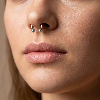 A titanium horseshoe septum ring in the septum piercing of a female model.