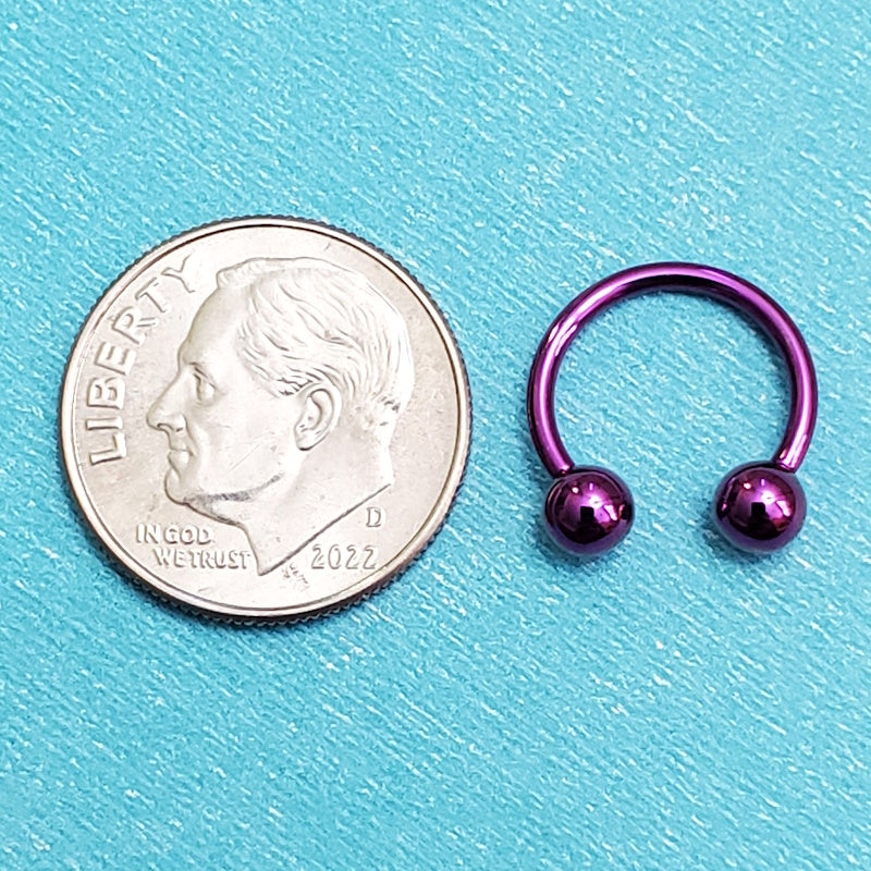 A titanium purple septum ring pictured on an aqua background next to a dime for a size comparison.