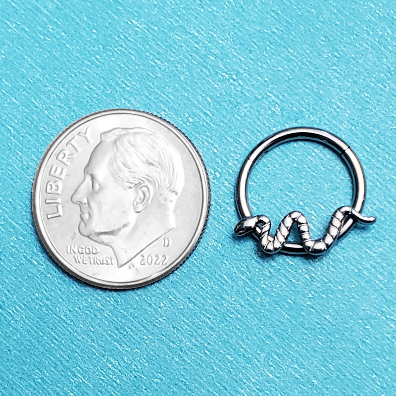 A titanium snake septum ring pictured on an aqua background next to a dime for a size comparison.