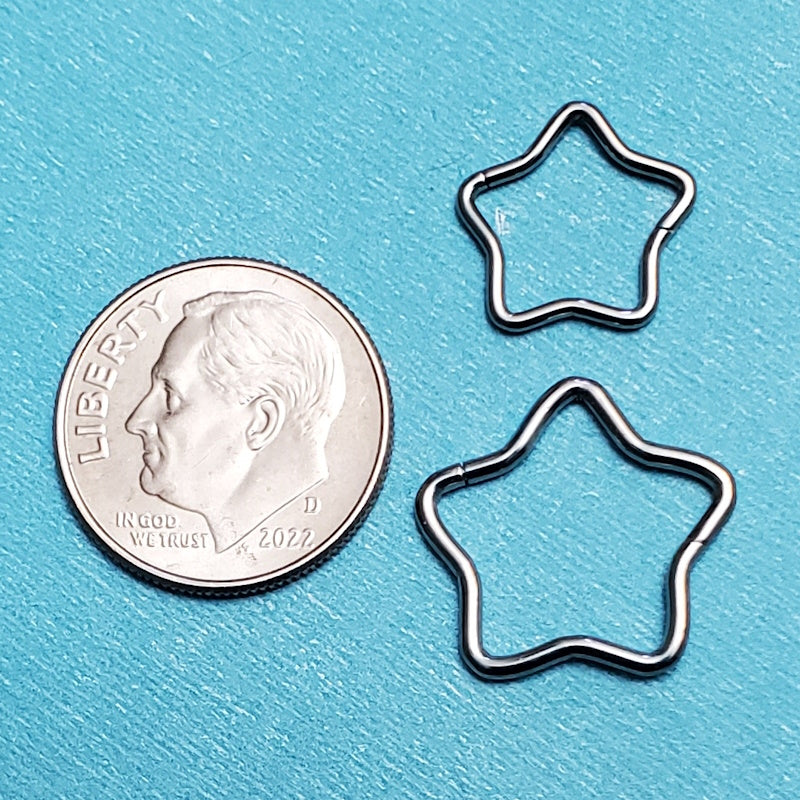 Two sizes of titanium star septum rings pictured on an aqua background next to a dime for a size comparison.