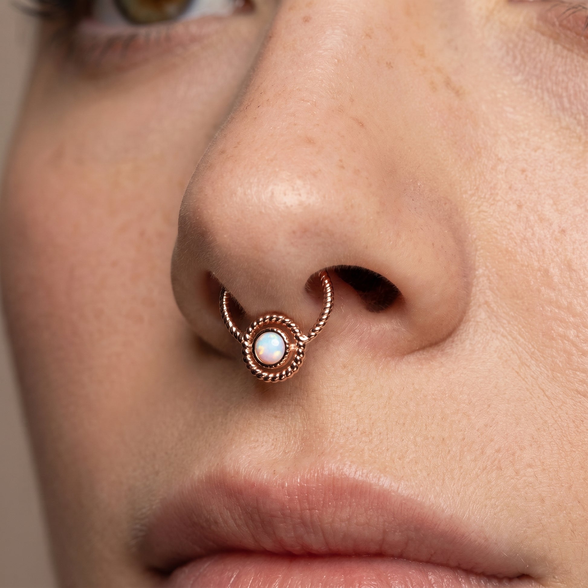 A twisted rope rose gold opal septum clicker pictured in the septum piercing of a female model.