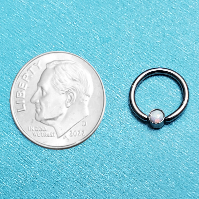 A white opal septum ring pictured on an aqua background next to a dime for a size comparison.